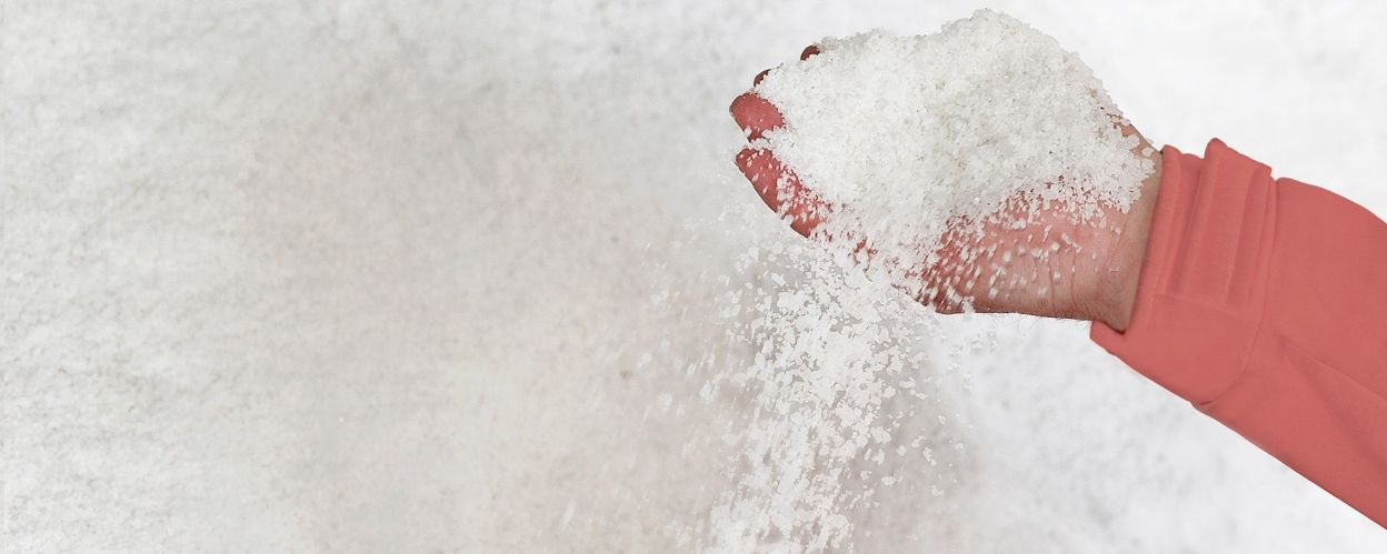 Von einer Hand rieselt Salz. Im Hintergrund ist ein Salzhaufen.